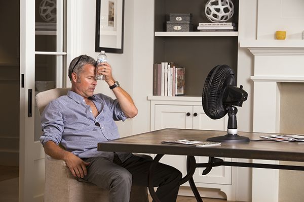 Overheating man sits in front of fan with cold bottle on forehead
