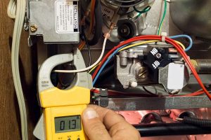 HVAC technician testing furnace wiring with a clamp meter during a furnace repair