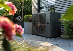 a heat pump outside of a house next to blooming flowers